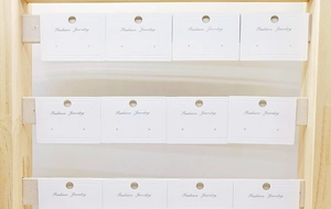 Close-up of white paper jewelry cards for earrings displayed on a wooden stand