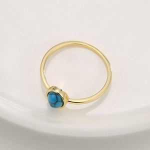 Bohemian gold ring with round blue turquoise stone on white ceramic plate