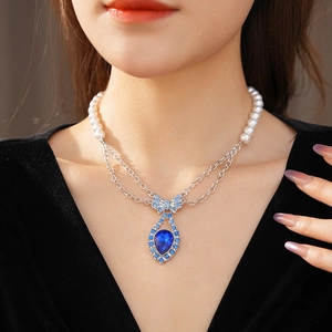 Close-up of double-layer pearl and silver chain necklace with a blue bow pendant on model