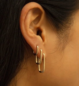 Three sizes of polished gold U-shaped huggie earrings worn together on a model ear