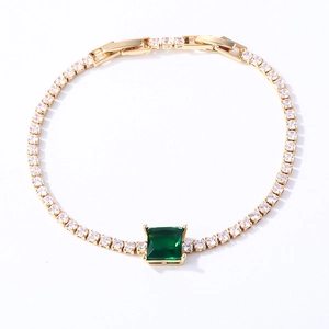 Macro shot of gold tennis bracelet with white zircons and emerald green square stone