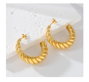 Detailed close-up of gold twisted croissant hoop earrings on a white textured stone base