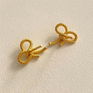 Macro shot of gold bow knot earrings with intricate rope texture and vintage finish