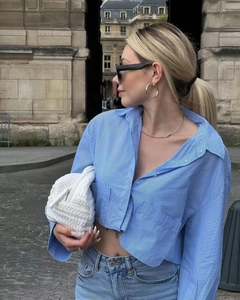 Street style shot of blue striped cropped shirt paired with a white woven clutch bag