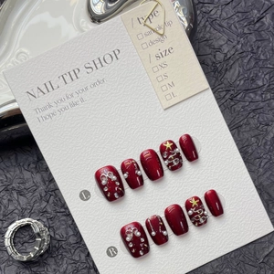 Détail de faux ongles de Noël rouges avec sapins argentés et perles sur une carte