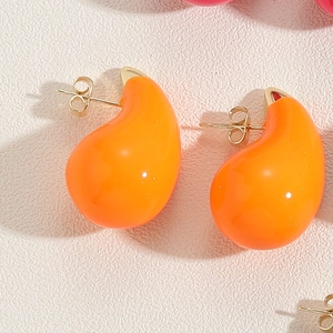 Macro view of teardrop enamel stud earrings in bright orange with golden metal backings