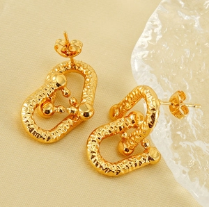 Macro detail of gold-plated U-shaped horseshoe earrings with hammered texture and sphere