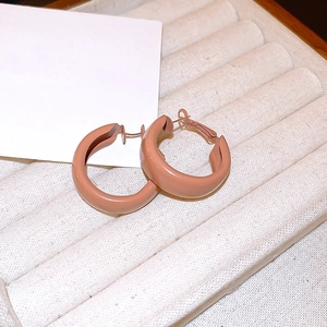 Close-up of minimalist C-shaped matte pink earrings on a beige velvet jewelry tray