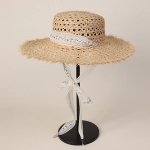 Detail of raffia straw hat featuring fringe brim and white floral lace ribbon