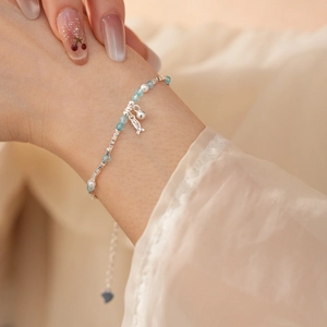 Detail of silver fish charm and pearls on a blue beaded bracelet worn on a wrist