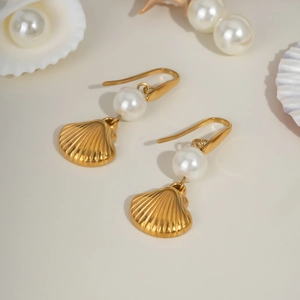Golden shell earrings with white pearl detail on a beige ocean themed background