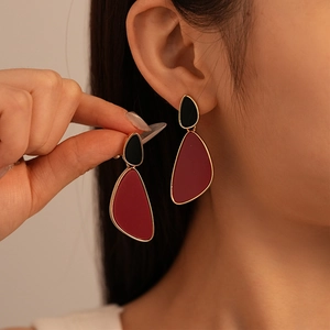 Close-up of model wearing geometric drop earrings in burgundy and black with gold edges