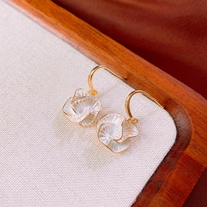 Macro view of gold-plated flower drop earrings with pearlescent petals on linen background