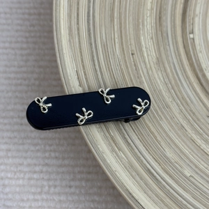 Close-up of a glossy black hair clip featuring four intricate silver metal bow accents
