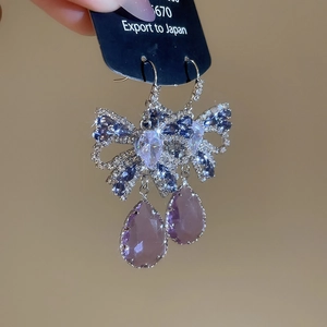 Macro detail of butterfly earrings featuring purple pear-cut crystals and blue zircons
