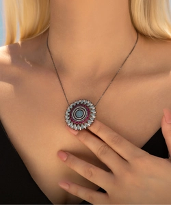 Detailed close-up of dark metal pendant featuring blue and magenta pavé-set gemstones