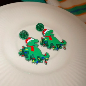 Detail of green glitter Christmas dinosaur earrings with Santa hats on a white plate