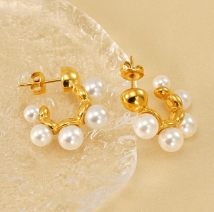 Detailed view of C-shaped gold pearl earrings on elegant champagne silk background