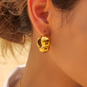 Close-up of three polished gold spheres stainless steel earrings on a female model