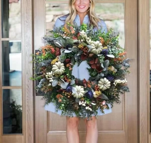 Large autumn wreath with eucalyptus and colorful pumpkins held by a person.