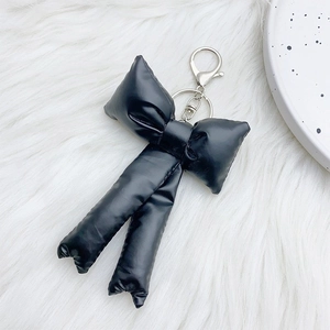 Detail view of a 3D puffy black bow keychain with silver metal clip on white plush surface