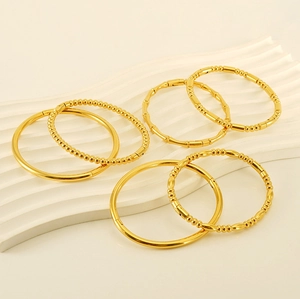 Detailed view of six assorted gold bamboo and beaded titanium steel bangles on a white tray