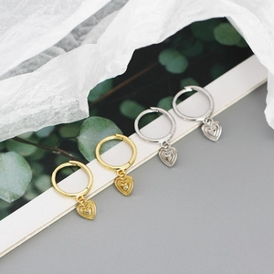 Detailed view of gold and silver heart-shaped pendant earrings on decorative background