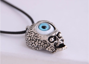 Macro shot of silver skull pendant featuring a large blue evil eye on black cord
