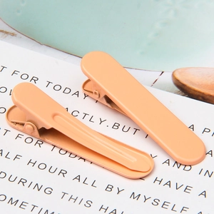 Detail view of two apricot matte metal duckbill hair clips on a minimalist background