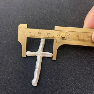Macro view of 28mm white cross baroque pearl measured with brass caliper on black surface