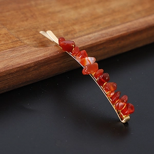 Macro shot of gold bobby pin with red agate stone fragments on a dark wooden tray