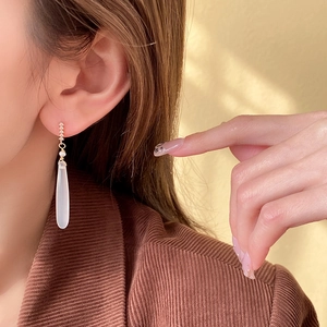 Close-up of model wearing gold zircon drop earrings with elegant white pendants