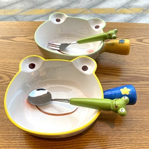 Detail of frog-themed ceramic bowls and stainless steel spoons on a wooden table