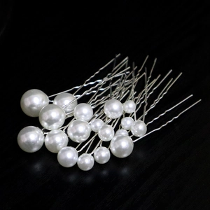 Detail shot of white pearl hair pins with silver metal U-shaped prongs on black surface