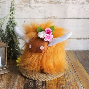 Highland cow plush with orange fur and floral crown on a rustic wooden surface
