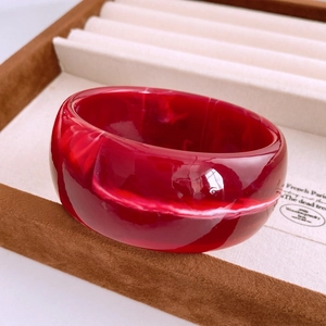 Détail macro d'un large bracelet en résine rouge avec texture marbrée sur velours
