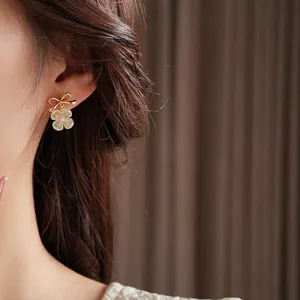 Elegant gold plated bow flower pearl drop earrings on female model with luxury fashion style