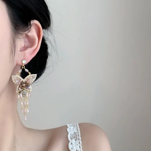 Détail des boucles d'oreilles papillon à pompons en zircon portées par un mannequin de profil