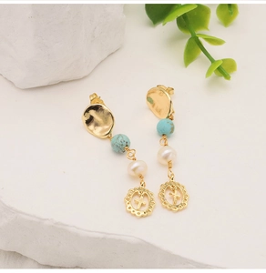 Détail de boucles d'oreilles croix dorées avec perles turquoise sur pierre blanche