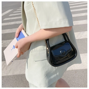 Street style view of a black glossy patent leather mini bag with gold chain strap