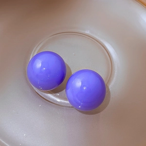 Close-up of bright purple acrylic ball stud earrings in a decorative beige bowl