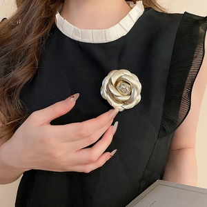 Close-up of a 3D layered gold rose brooch pinned on a black sleeveless top with white trim