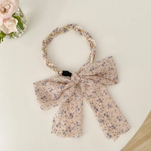 Detail of floral headband with faux pearls, golden chain, and a large pink bow decoration