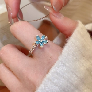 Detail of blue enamel flower ring with silver twisted band on hand with a soft knit sweater