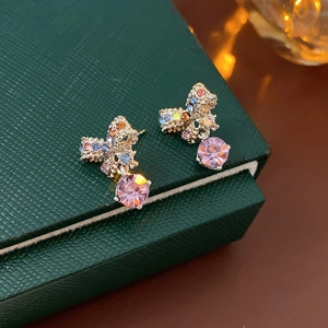 Detail of gold bow earrings with colorful pavé stones and a large pink crystal drop