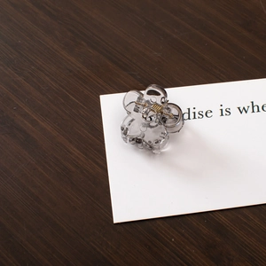 Close-up of a small transparent floral hair claw clip on a white card with wooden background