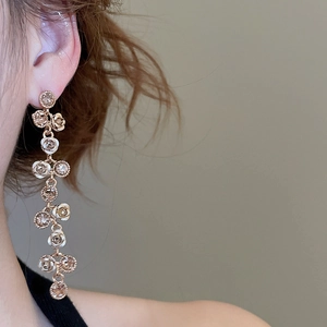 Detail shot of elegant rose-shaped long tassel earrings with sparkling rhinestones in gold