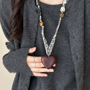 Close-up of heart-shaped fabric pendant necklace with geometric beads on a gray cardigan