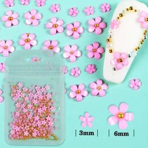 Detail of pink 3mm and 6mm 3D nail art flowers with gold beads on a blue backdrop