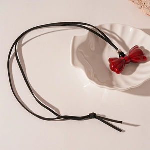 Detail of red resin bow pendant on black cord necklace with metallic bead accent